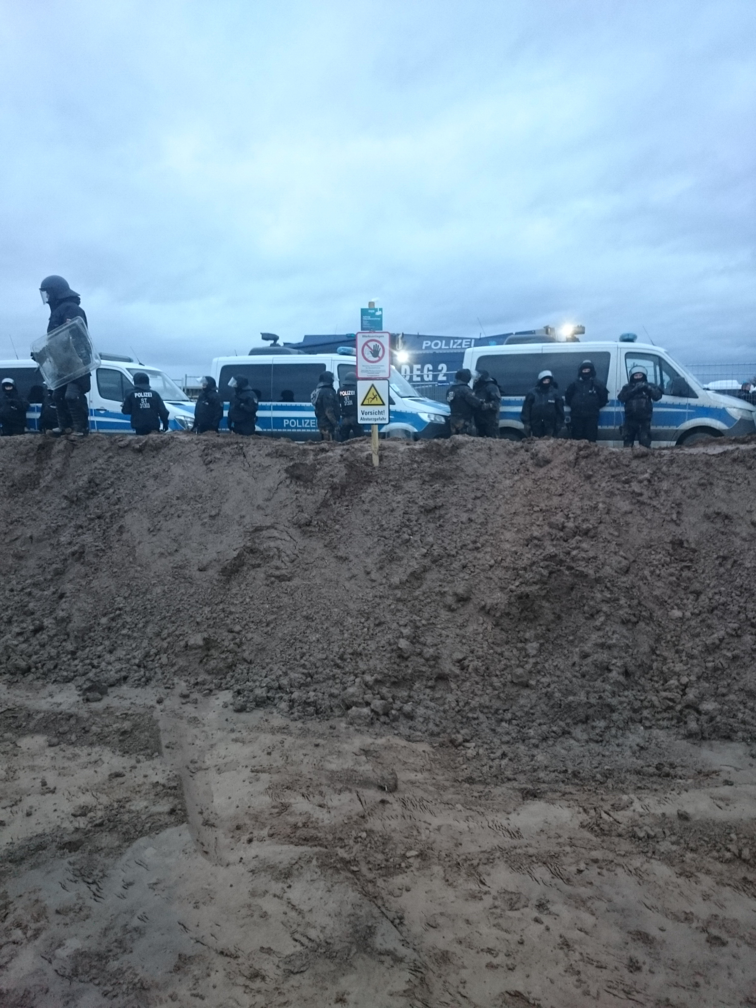 Erdwall mit Hinweisschild und dahinter Polizeisperre