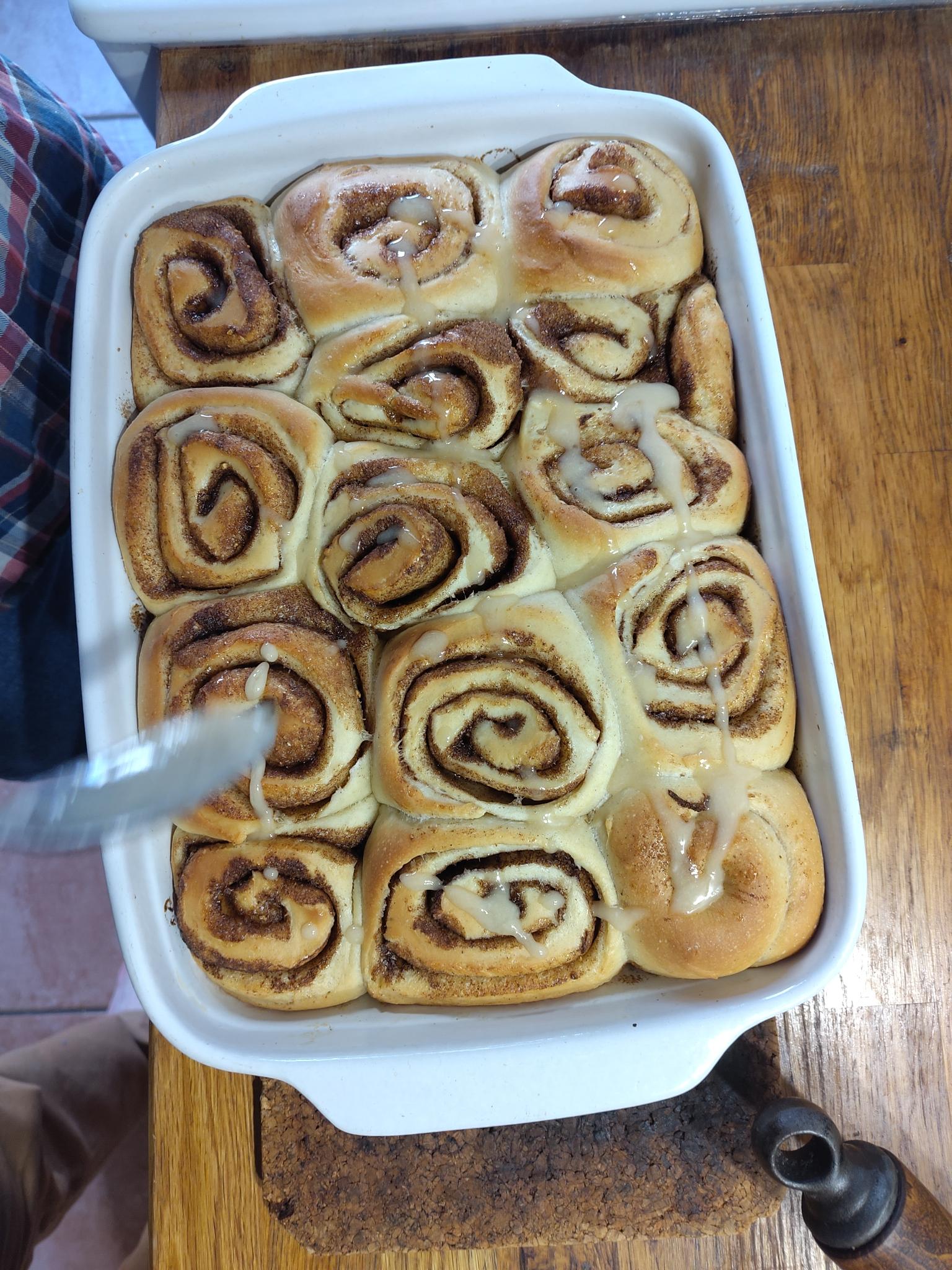 Warme Zimtschnecken die gerade mit Zuckerguss bestrichen werden
